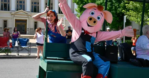 A pig mascot and a woman in costume ride on a float.