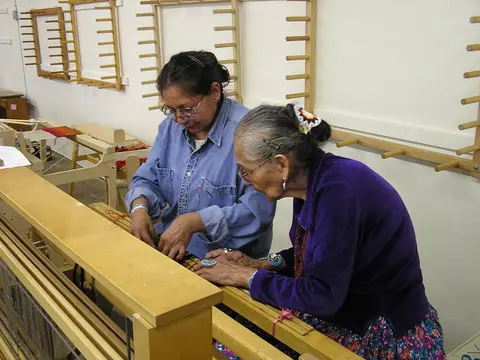 Two women work together at a large wooden loom.