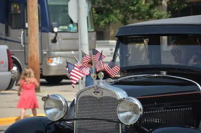 A vintage car decorated with American flags is parked on a street.