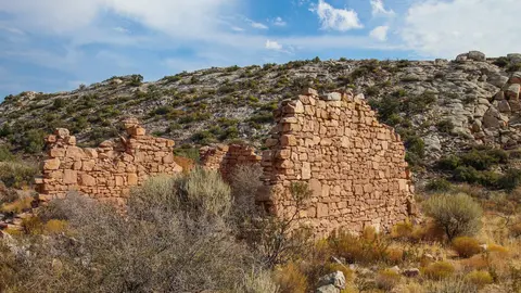 Stone ruins stand in a desert landscape under a blue sky.