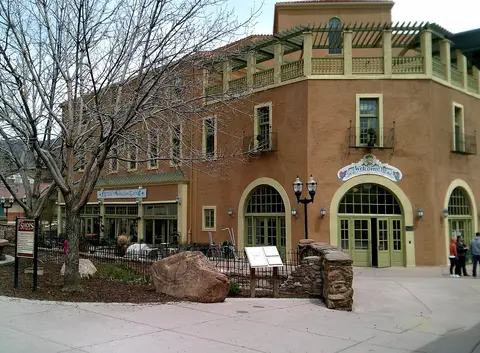 A large tan commercial building with green trim and a patio area surrounded by trees.