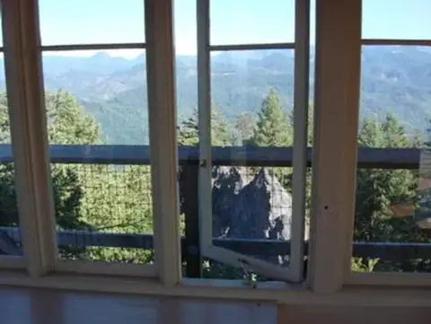 A view of mountains and trees looking through open windows from an interior.