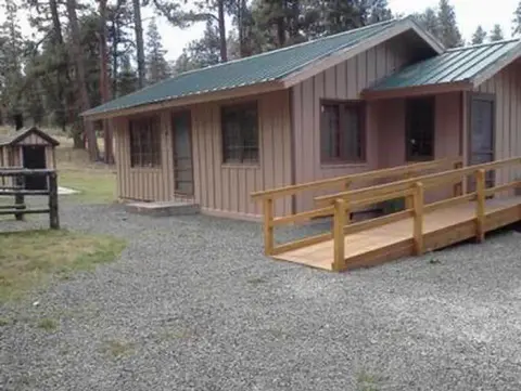A single-story wooden cabin with a wheelchair ramp outside in a wooded area.