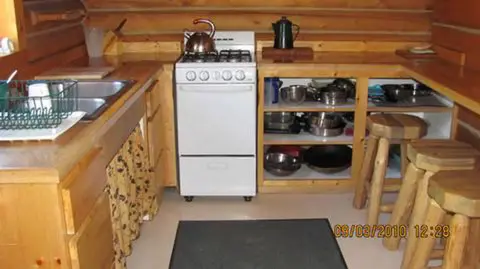 A rustic wooden kitchen with a stove, sink, and stools.