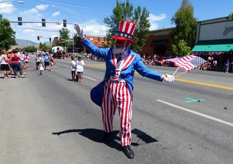 A person dressed as Uncle Sam waves in a street parade.