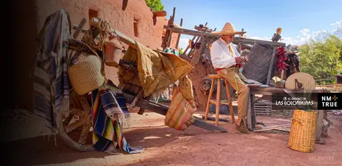 A man wearing a sombrero sits on a stool outside working by a rustic cart.