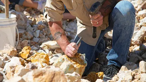 A person uses a hammer and chisel to break rocks outdoors.