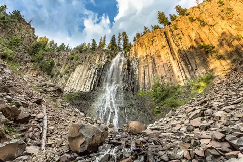 A waterfall flows down a rocky cliff surrounded by trees.