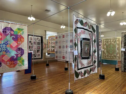 Quilts displayed on metal racks inside a room with hardwood floors.