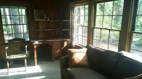 An interior room with a wooden desk, chair, and sofa near large windows.
