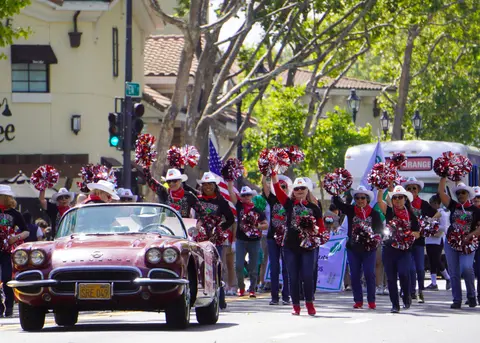 A group of women with pom-poms participate in a parade alongside a vintage convertible.