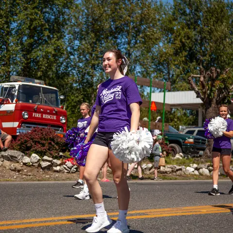 A young woman holding pom-poms walks in a parade.