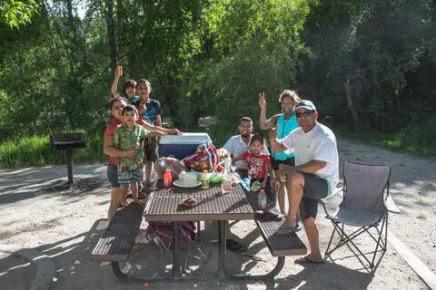 A family having a picnic at an outdoor table in a wooded park.