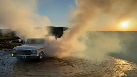 A pickup truck creates a large cloud of smoke while doing a burnout at sunset.