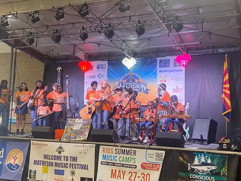 A group of young musicians perform on a stage with festival banners.