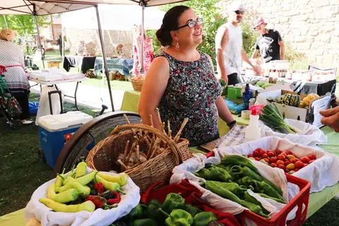 A woman stands behind a table selling produce at an outdoor market.