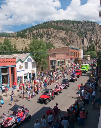 An elevated view of a parade moving down a town street with mountains in the background.