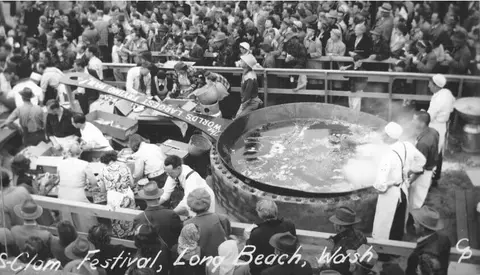 Black and white photograph of a large crowd and cooking setup at a festival.