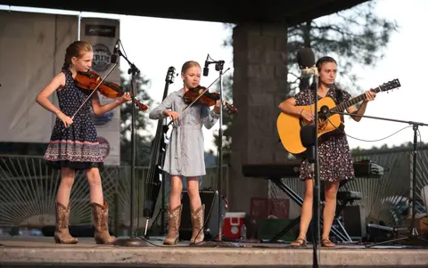 Three young musicians perform on an outdoor stage.