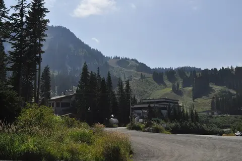 A view of a mountain resort with buildings, trees, and a road under a blue sky.