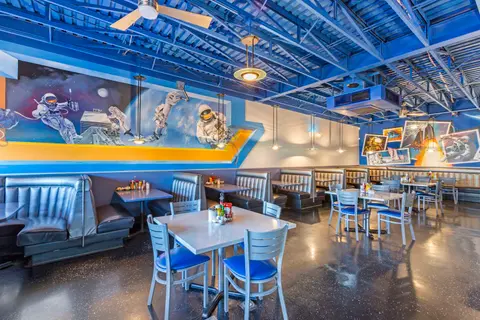 An interior view of a restaurant with space-themed wall murals and blue accents.