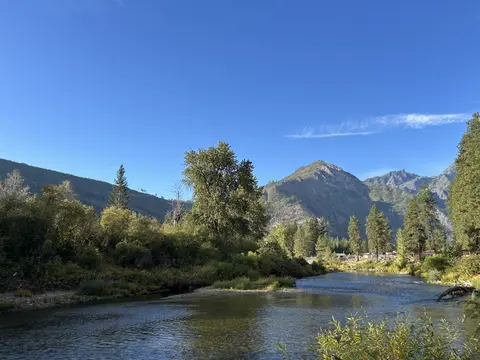 A scenic landscape shows a river flowing past green trees toward distant mountains under a blue sky.
