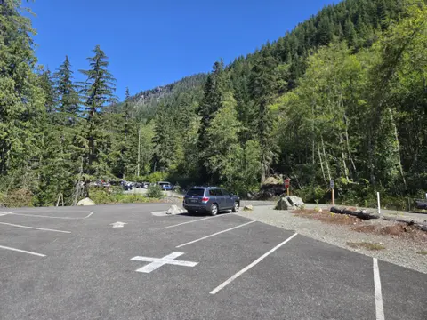 A parking lot surrounded by a dense forest and mountains under a blue sky.