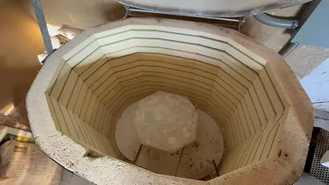 A pottery kiln opened from above showing the inside lining and a stone support.