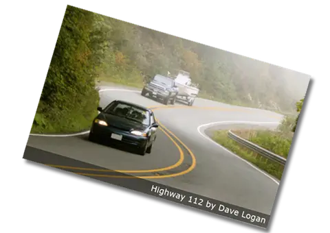 Cars drive along a winding road surrounded by trees.