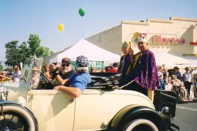 People riding in a vintage car during an outdoor parade.