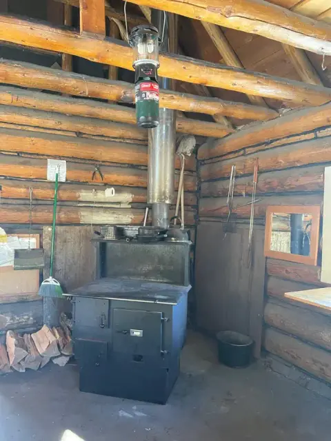 The interior of a rustic log cabin with a wood-burning stove and hanging lantern.