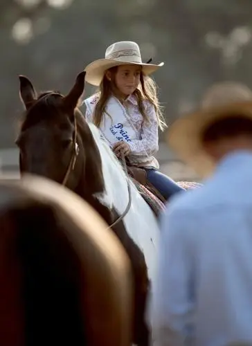 A young girl in a cowboy hat rides a horse.
