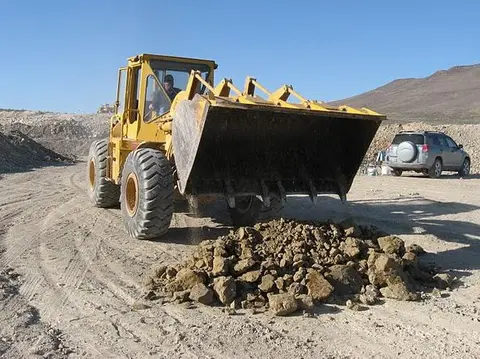 A yellow loader dumps a pile of rocks on a dirt ground.
