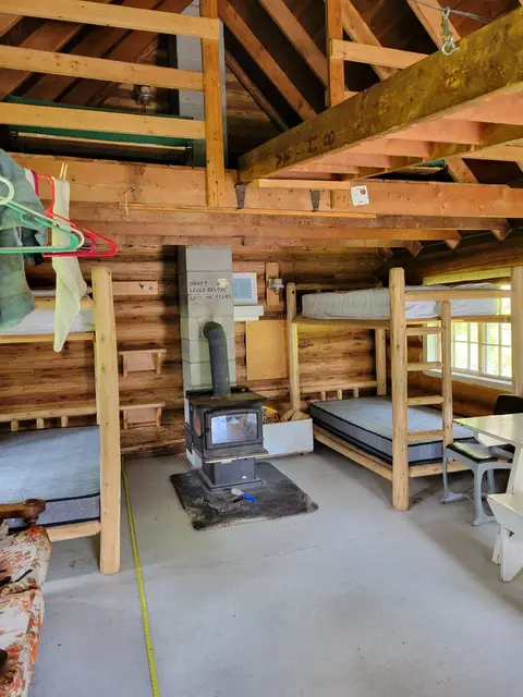 A rustic interior cabin with bunk beds and a wood stove.