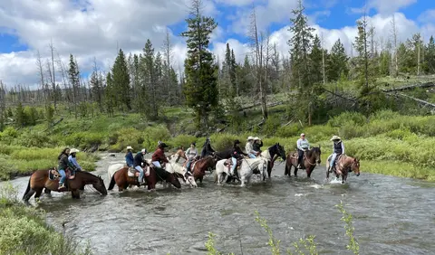 A group of people ride horses through a shallow river.