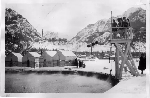 A person dives into an outdoor pool surrounded by snow and mountains.