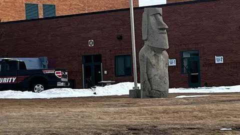 A stone moai statue stands outside a brick building with a security vehicle parked nearby.