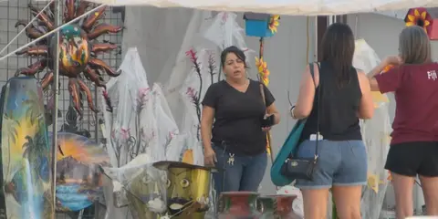 People at an outdoor vendor booth with crafts and art.