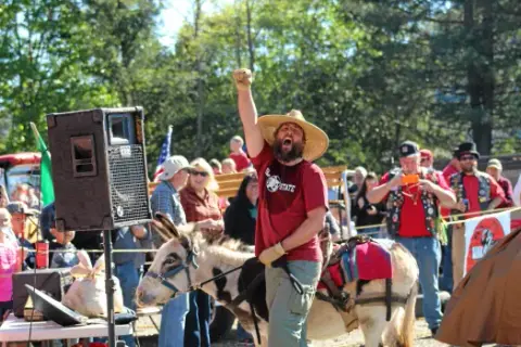 A man wearing a straw hat and raising his fist while standing next to a donkey.