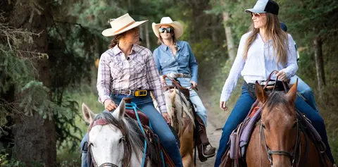 Three women ride horses along a wooded trail.