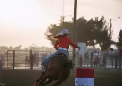 A person riding a horse around a barrel in an arena.