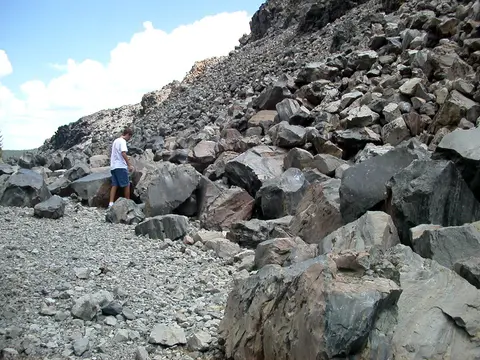 A person standing among large boulders and rock debris on a hillside.