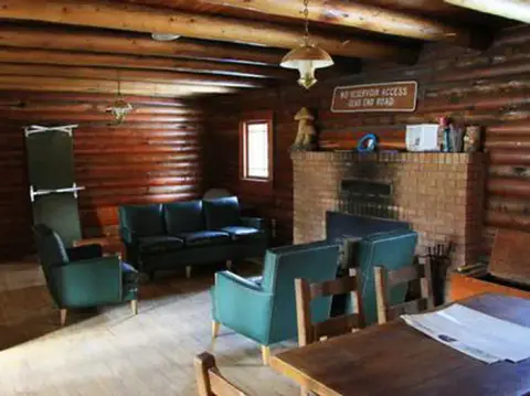 An interior view of a log cabin with a brick fireplace, sofa, and armchairs.