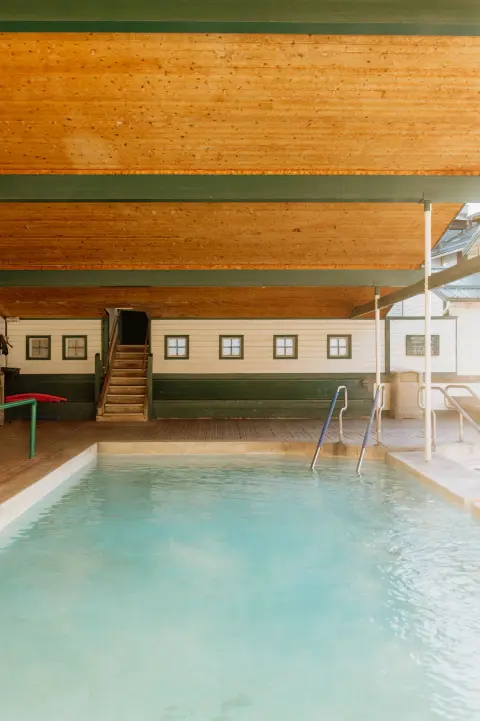 A swimming pool inside a wooden building with stairs and windows along the back wall.