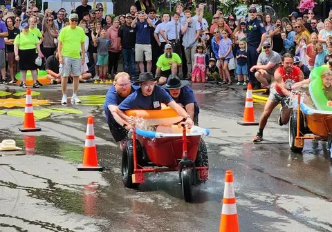 People race a makeshift vehicle down a wet street while a crowd watches.