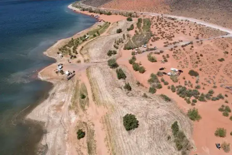 An aerial view of a lake shore with sparse vegetation and sandy terrain.