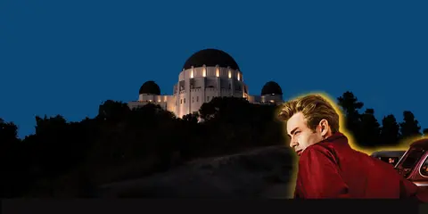 A person stands near a large illuminated building on a hill at night.