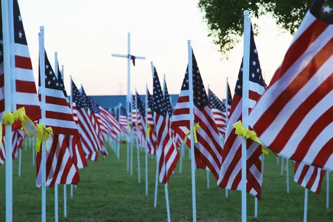 A field of American flags displayed on poles with yellow ribbons.