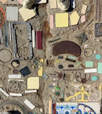 A detailed view of a mosaic embedded in concrete containing various tiles and found objects.