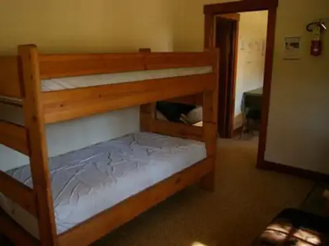 A wooden bunk bed stands inside a room with a doorway leading to another area.